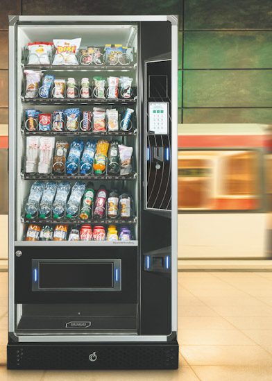 Máquina de snacks e bebidas frias cheia de produtos, num espaço de passagem